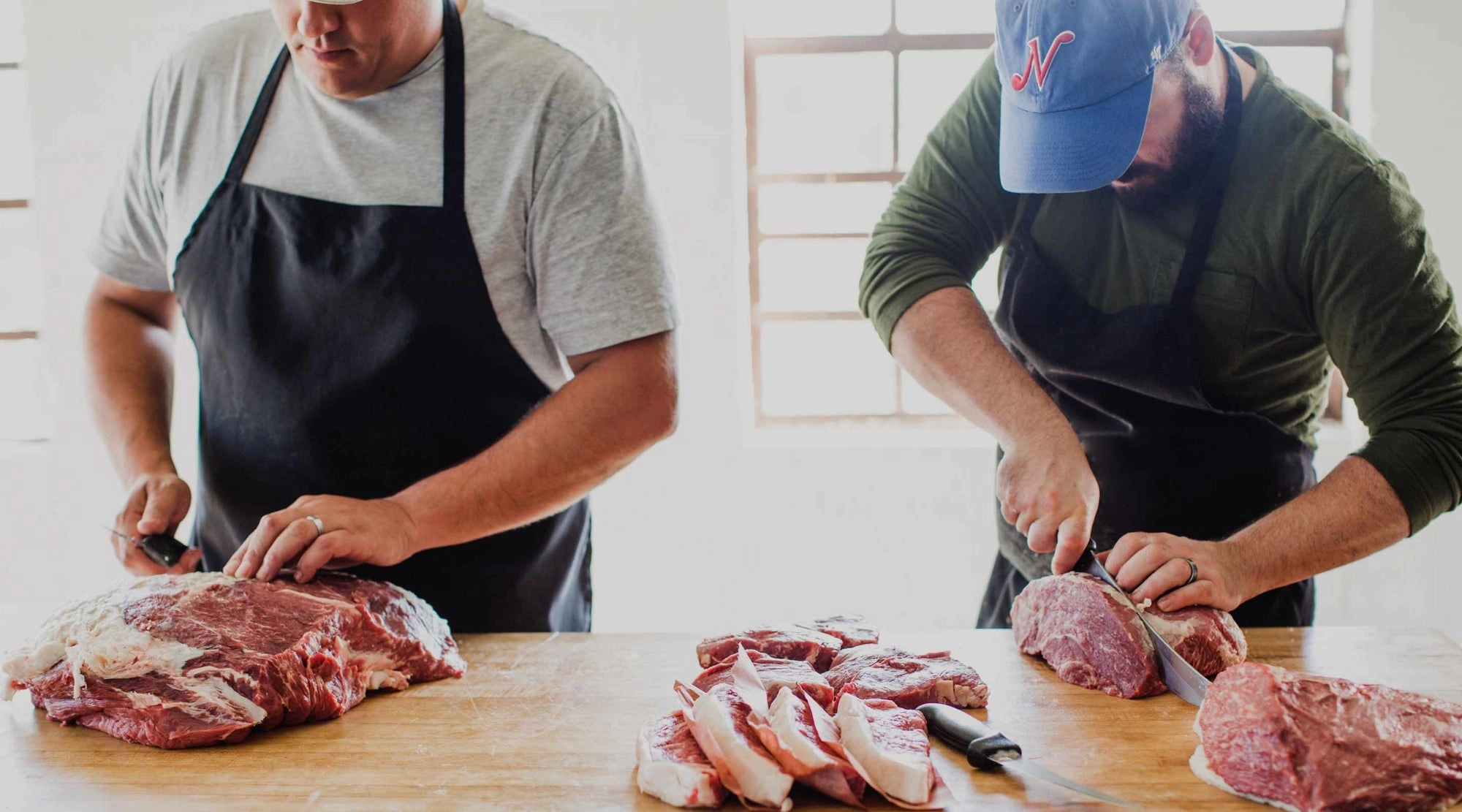 Two butchers breaking down beef on a wooden block