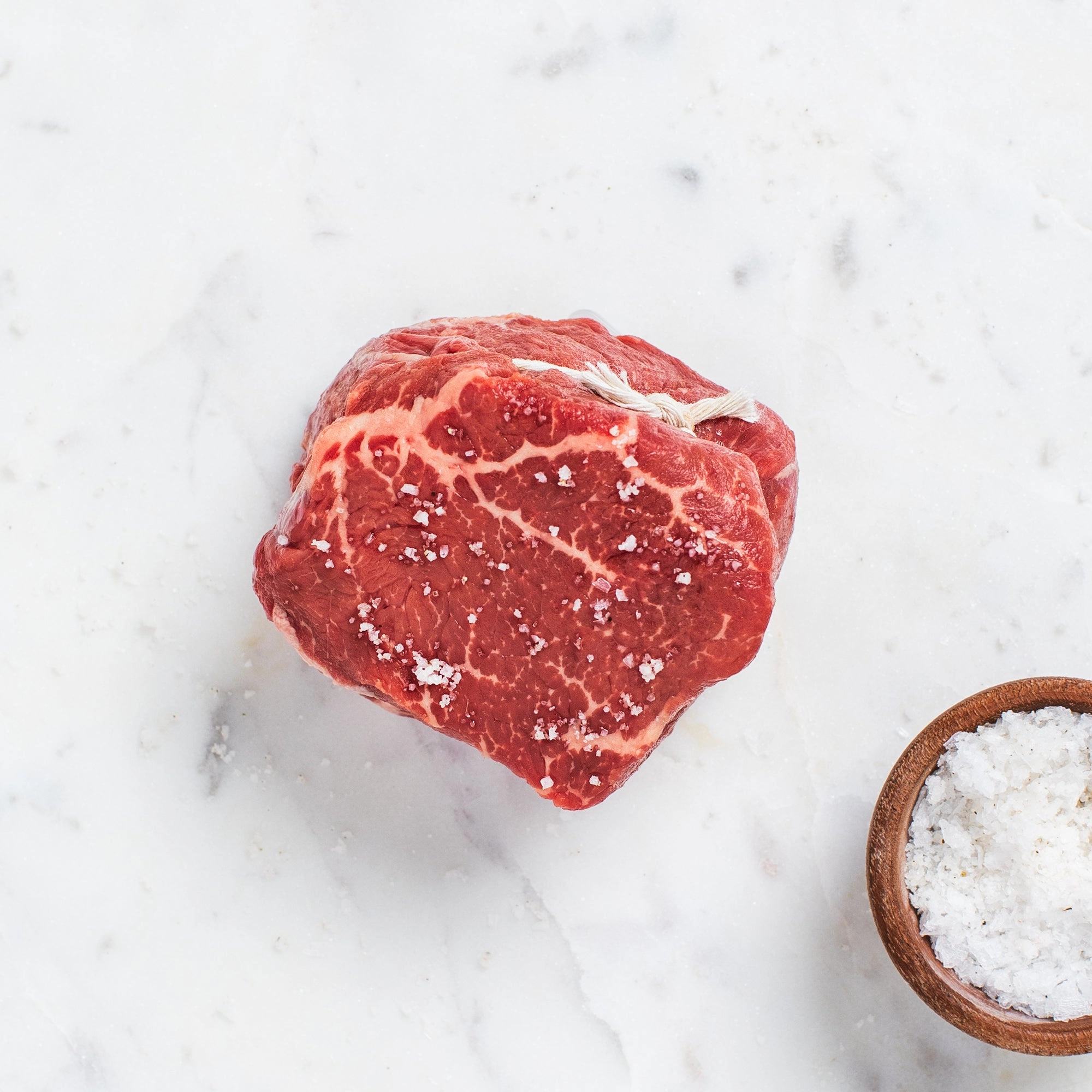 Dry aged beef cut seasoned with flaky salt on white marble