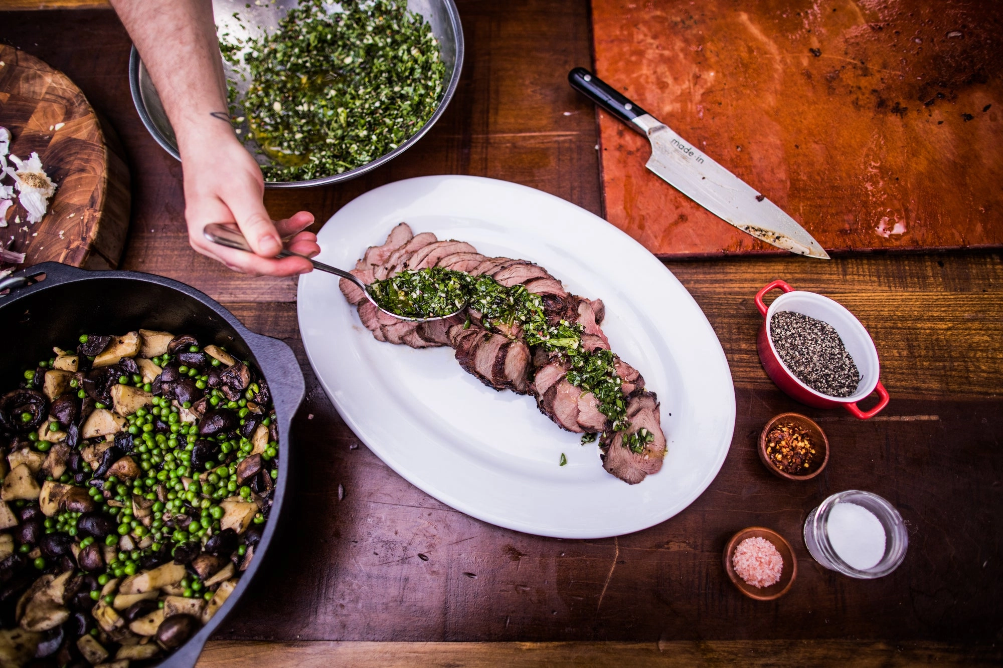 Sliced roast with chimichurri on a platter, beside a chef's knife