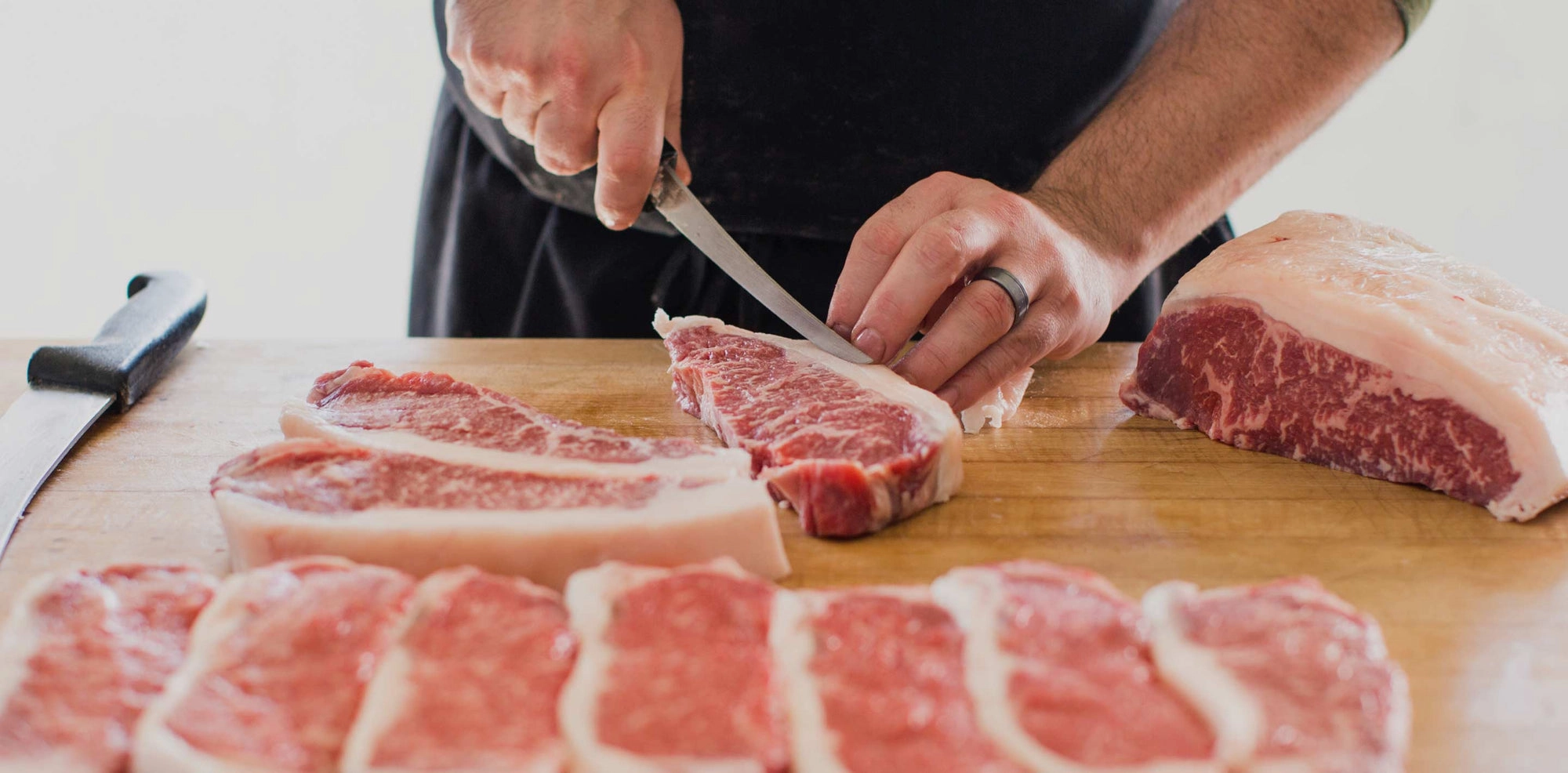 Butcher hand-cutting beef steaks on a wooden block